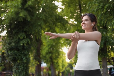 Young woman with wireless earphones doing morning exercise outdoors