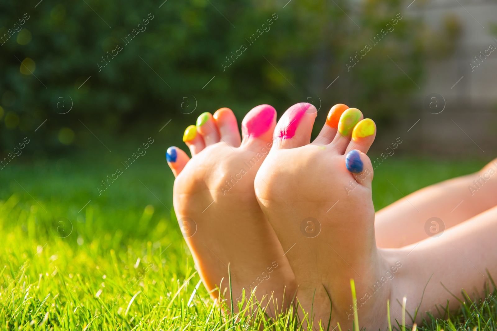 Photo of Teenage girl with painted toes on green grass outdoors, closeup