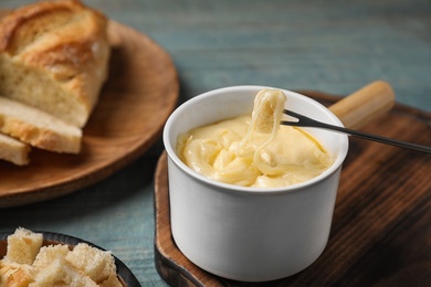 Pot of tasty cheese fondue and fork with bread on blue wooden table