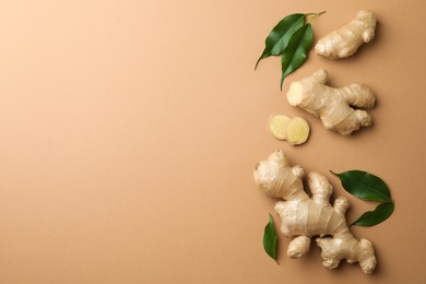 Photo of Fresh ginger with green leaves on light pale brown background, flat lay. Space for text