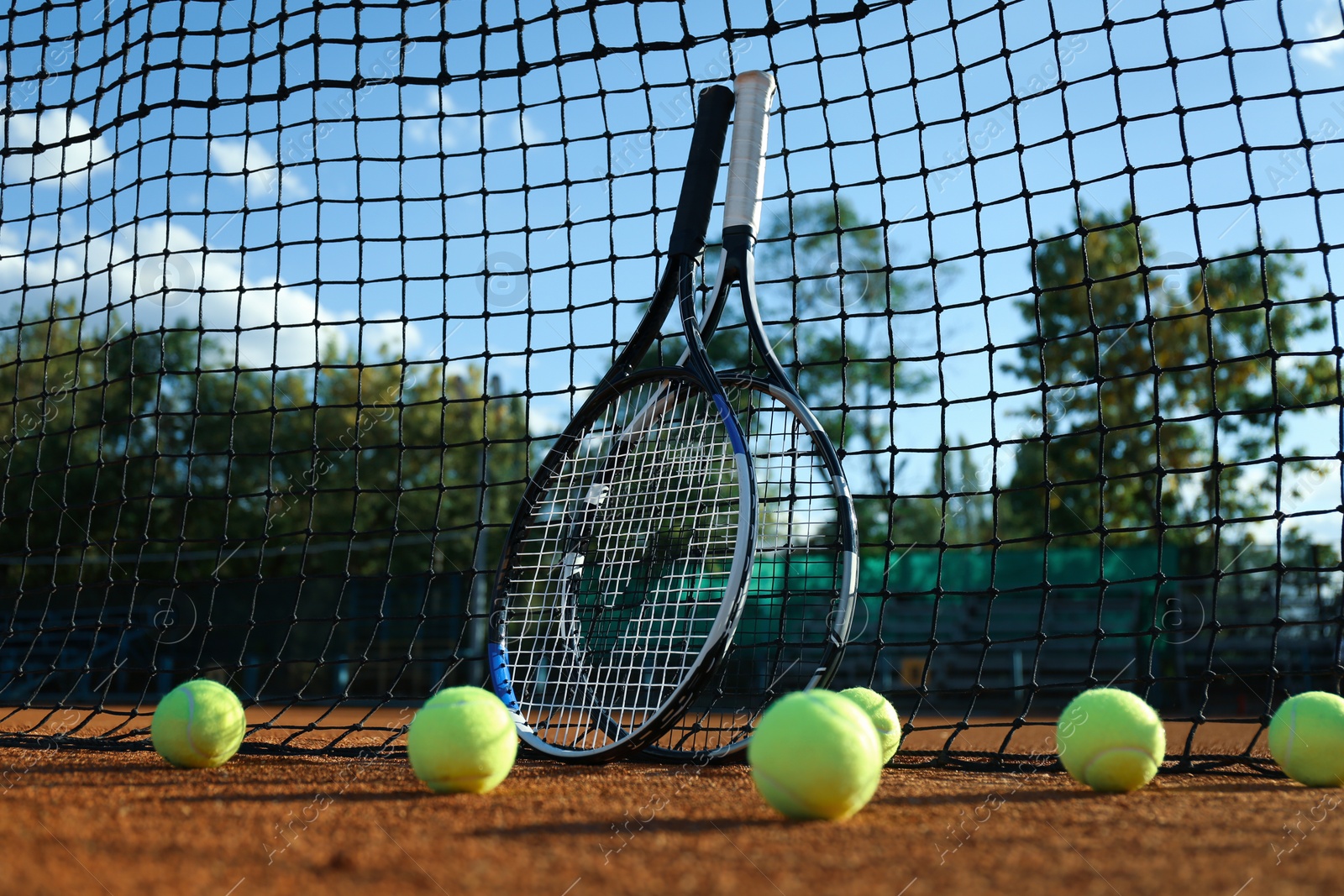 Photo of Tennis balls and rackets near net on clay court