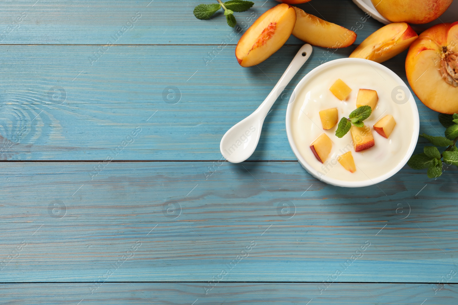 Photo of Delicious yogurt with fresh peach and mint on light blue wooden table, flat lay. Space for text