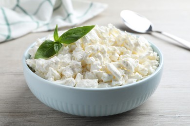 Photo of Fresh cottage cheese with basil in bowl on light wooden table, closeup