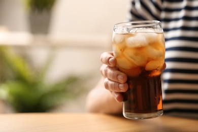 Photo of Woman holding glass of cola with ice at table, closeup. Space for text