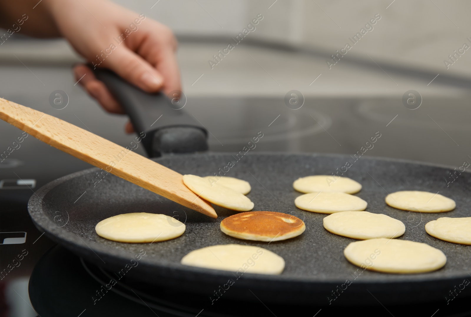 Photo of Woman turning cereal pancake with spatula on stove, closeup