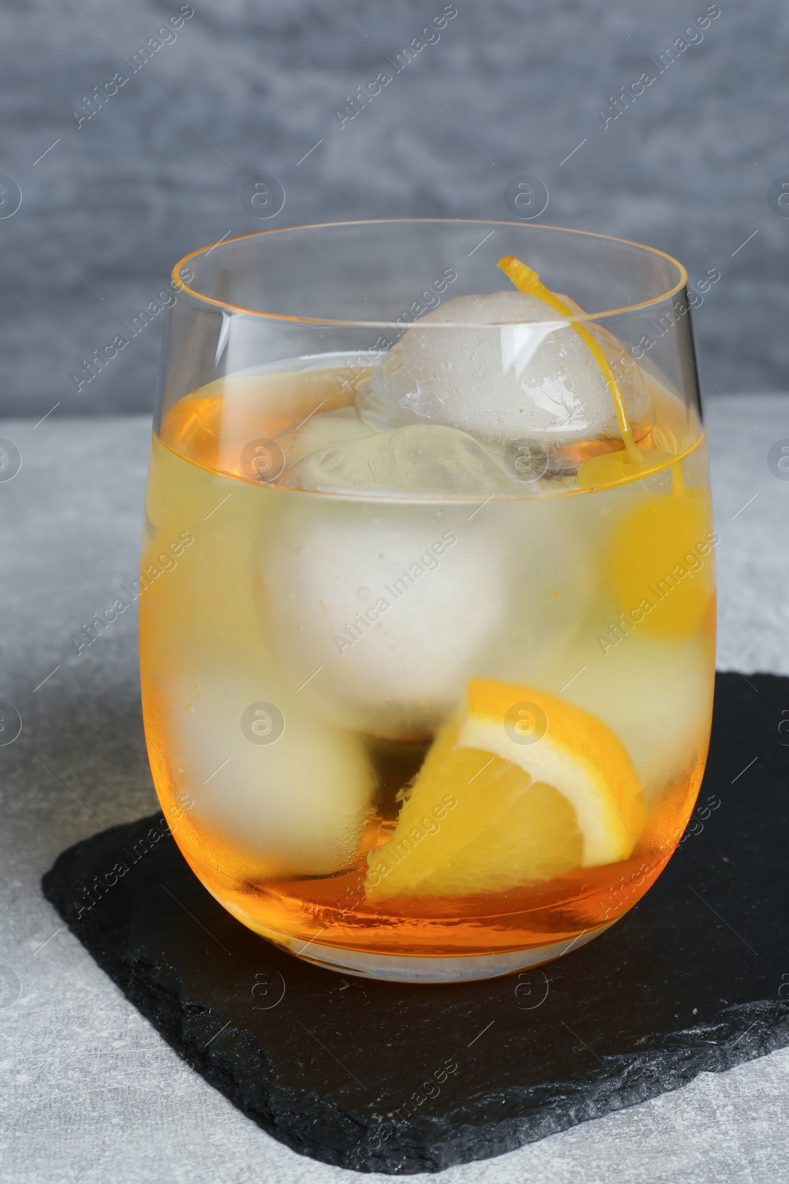 Photo of Delicious cocktail with orange, yellow cherry and ice balls on grey table
