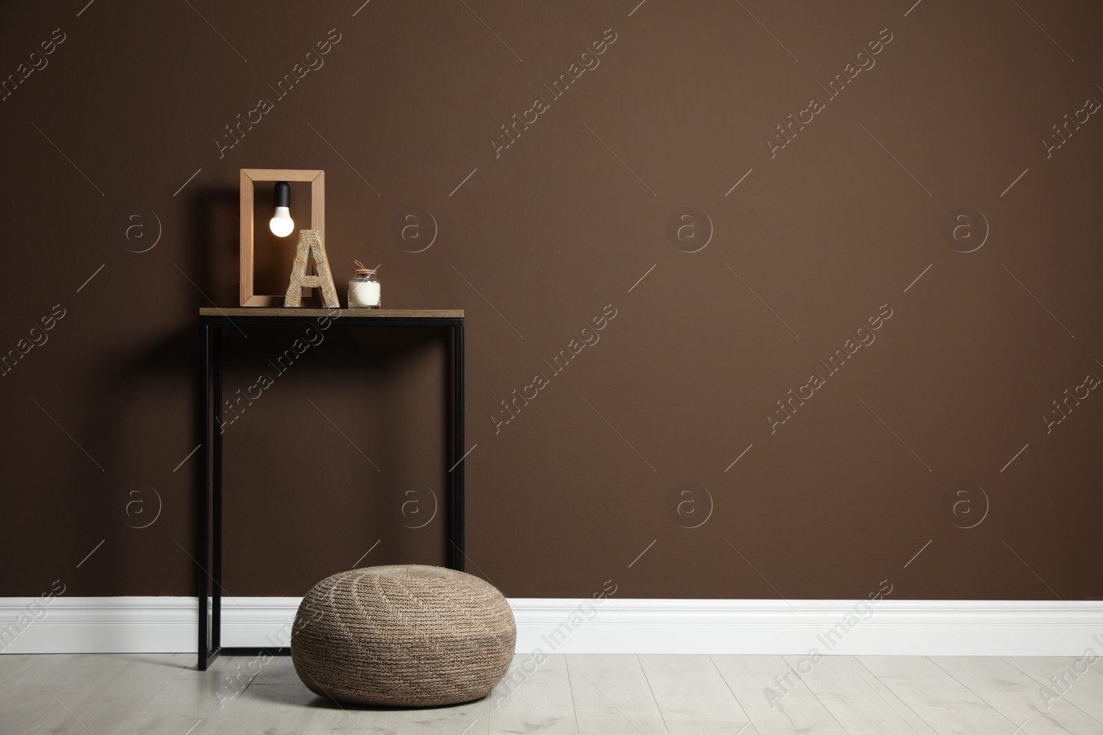 Photo of Comfortable knitted pouf and table with decor elements near brown wall indoors, space for text. Interior design