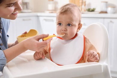 Photo of Mother feeding her cute little baby in kitchen