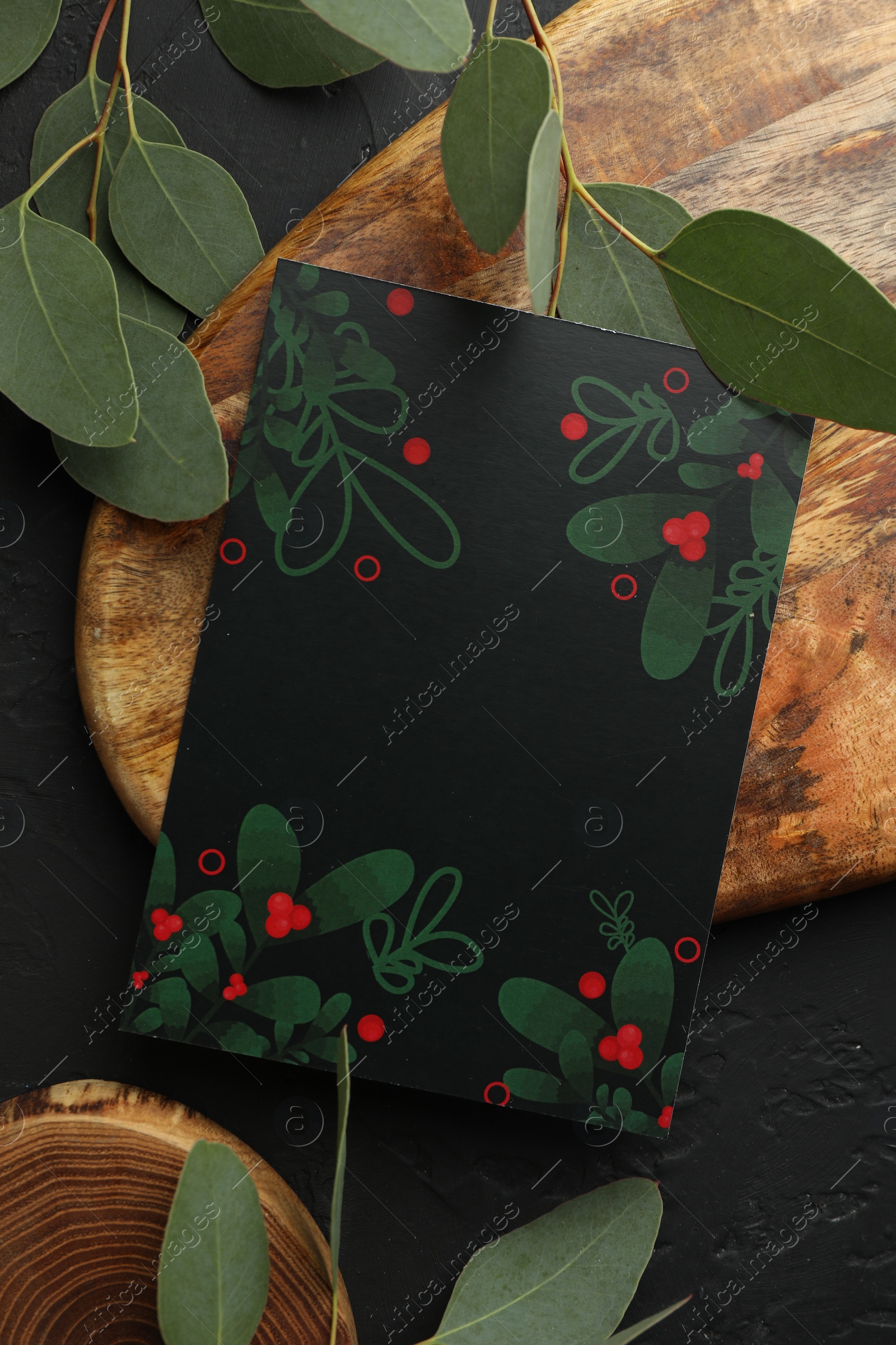 Photo of Blank invitation card and green leaves on black textured background, flat lay. Space for text