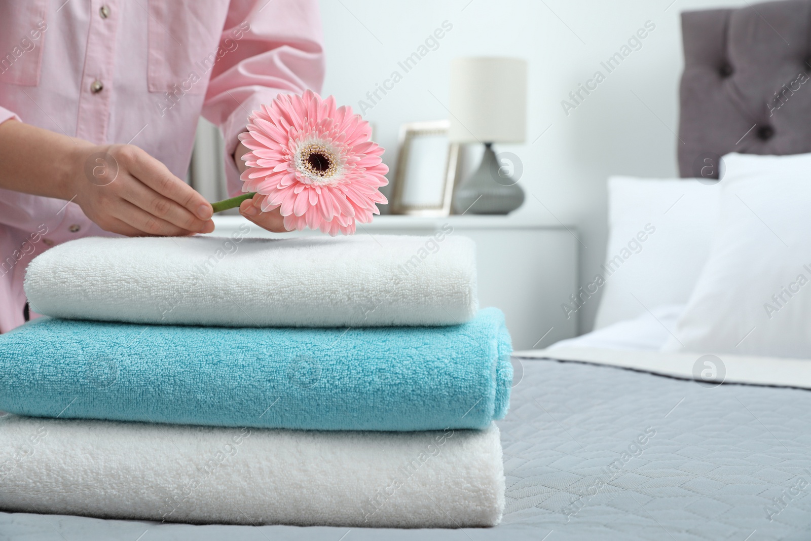 Photo of Woman putting flower on stack of clean towels in bedroom. Space for text