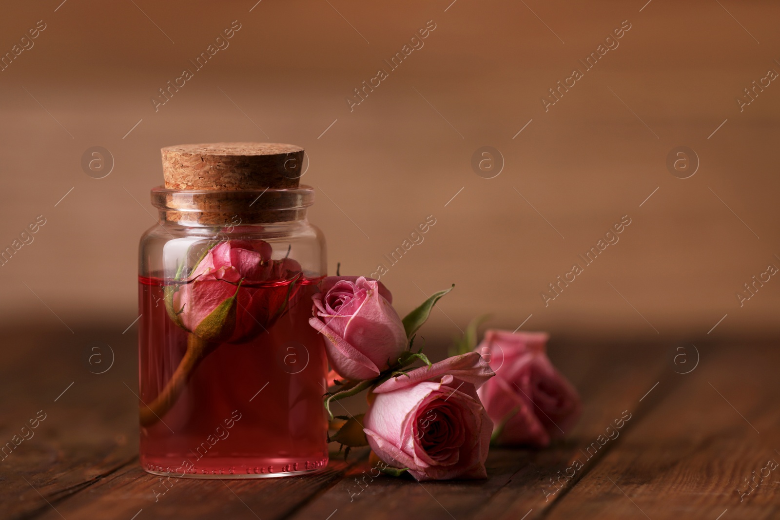 Photo of Bottle of essential rose oil and flowers on wooden table, space for text