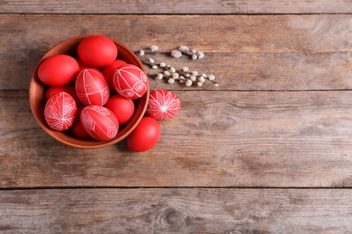 Bowl with red painted Easter eggs on wooden background, top view. Space for text