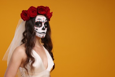 Photo of Young woman in scary bride costume with sugar skull makeup and flower crown on orange background, space for text. Halloween celebration