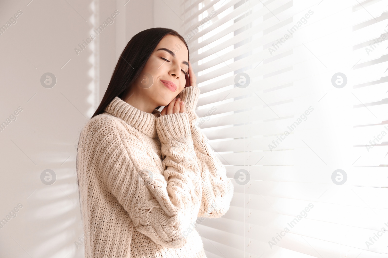Photo of Young woman wearing warm sweater near window at home. Winter season