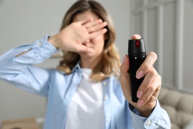 Photo of Young woman covering eyes with hand and using pepper spray at home