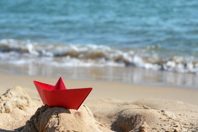 Photo of Red paper boat near sea on sunny day, space for text