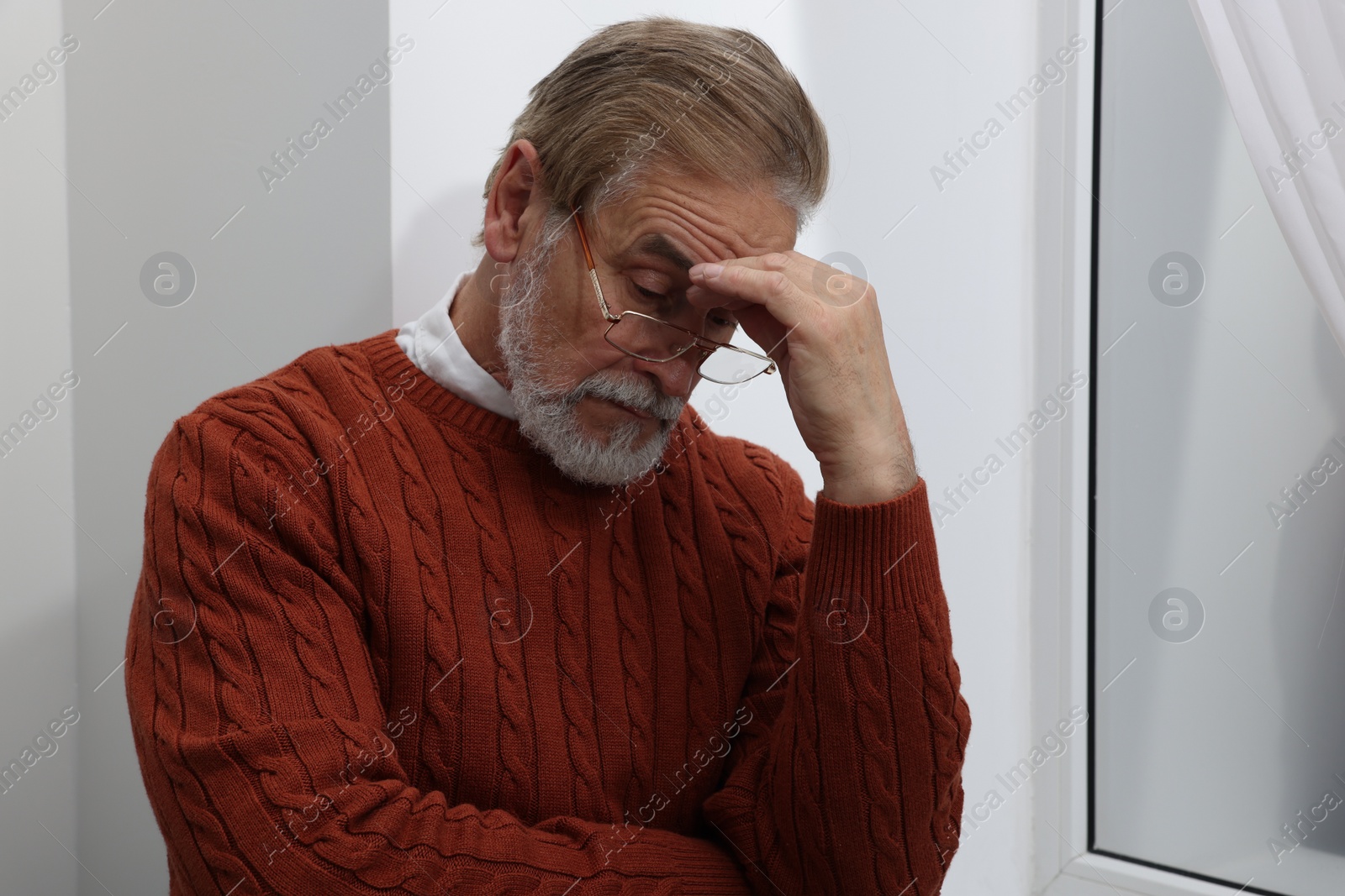 Photo of Upset senior man near window at home. Loneliness concept