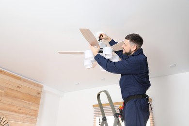 Electrician with screwdriver repairing ceiling fan indoors. Space for text