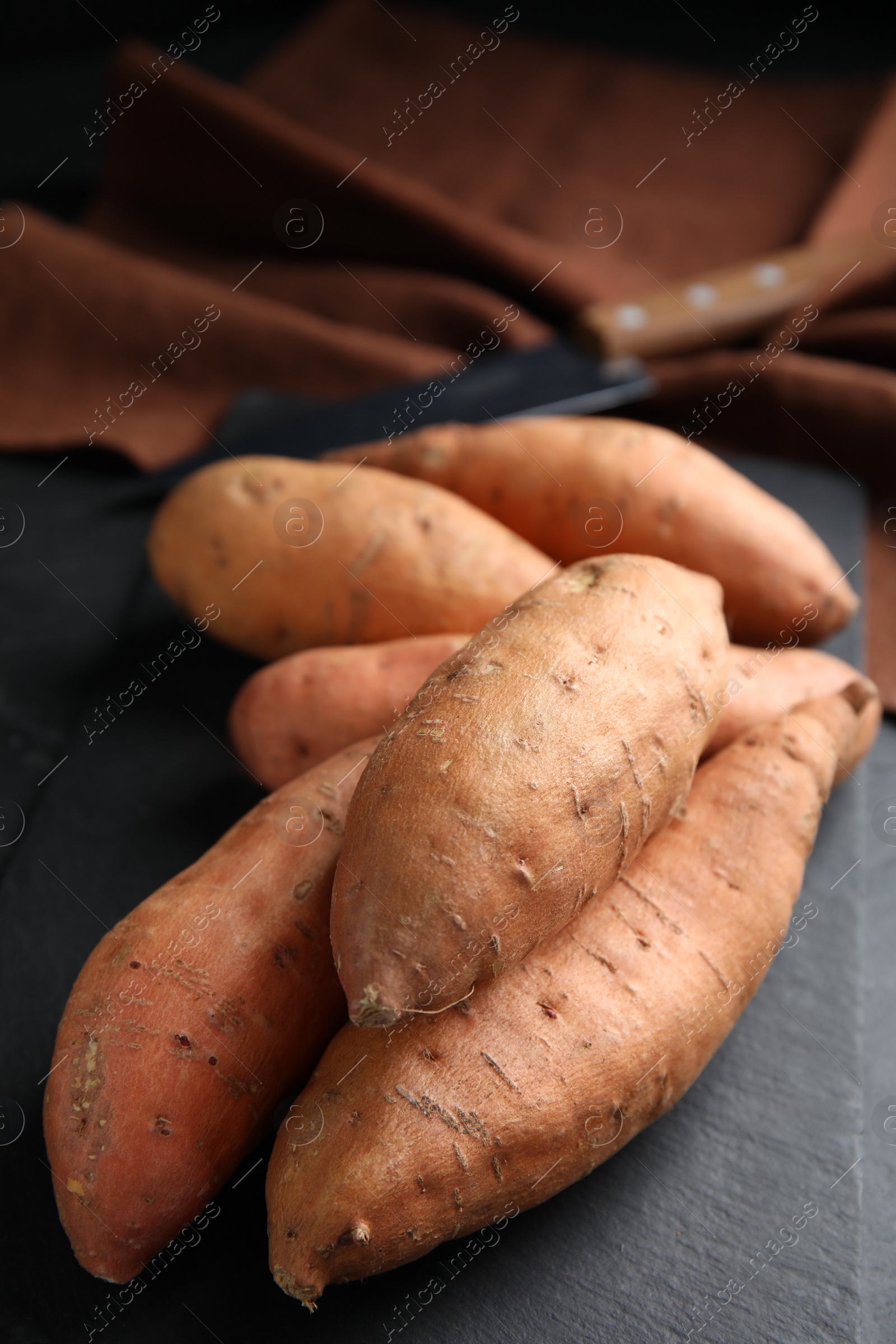 Photo of Heap of whole ripe sweet potatoes on black table