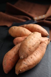 Photo of Heap of whole ripe sweet potatoes on black table