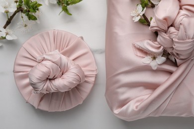 Photo of Furoshiki technique. Gifts packed in pink fabric and beautiful flowers on white marble table, flat lay