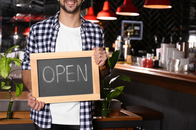 Photo of Young business owner holding sign OPEN in his cafe, closeup. Space for text