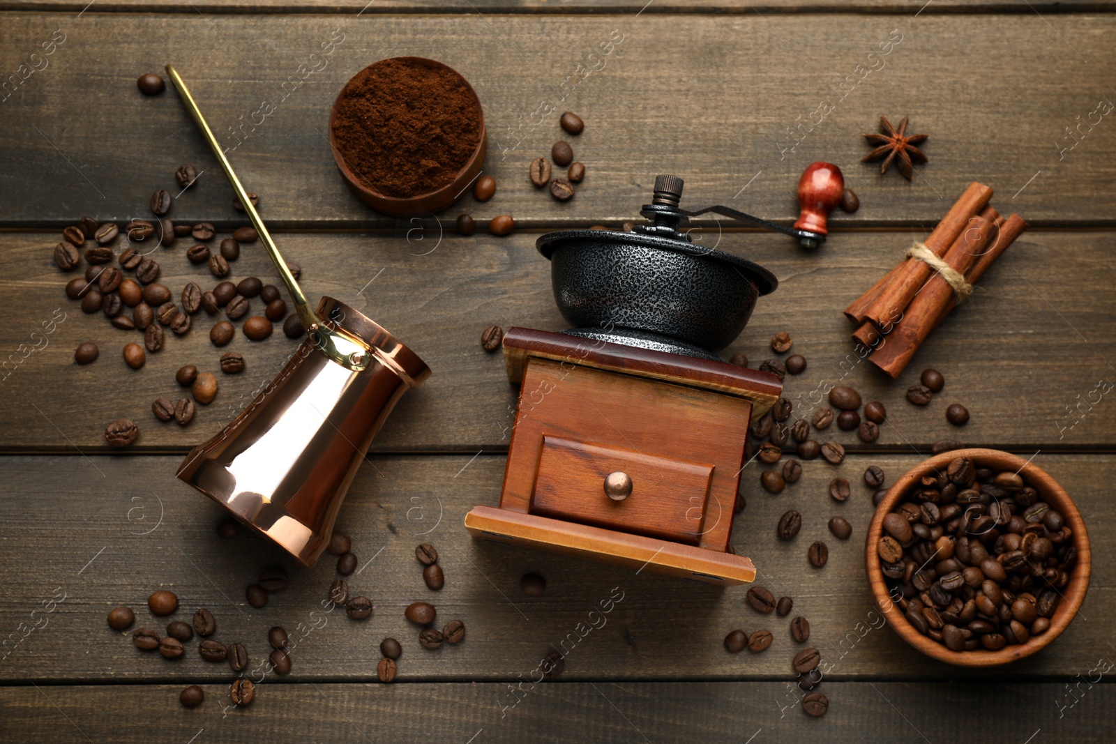 Photo of Vintage manual coffee grinder, beans, powder, cinnamon and jezve on wooden table, flat lay