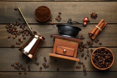 Vintage manual coffee grinder, beans, powder, cinnamon and jezve on wooden table, flat lay