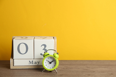 Photo of Wooden block calendar and alarm clock on table against yellow background. Space for text