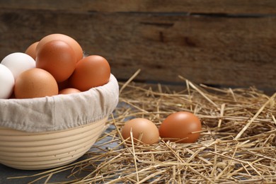 Fresh chicken eggs in bowl and dried straw on grey wooden table. Space for text