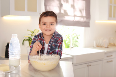 Cute little boy cooking dough in kitchen at home