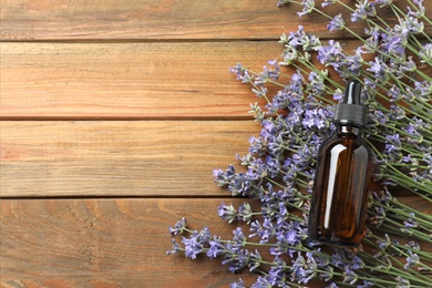 Photo of Bottle of essential oil and lavender flowers on wooden background, top view. Space for text