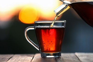 Photo of Pouring delicious tea into glass cup on wooden table against blurred background, closeup