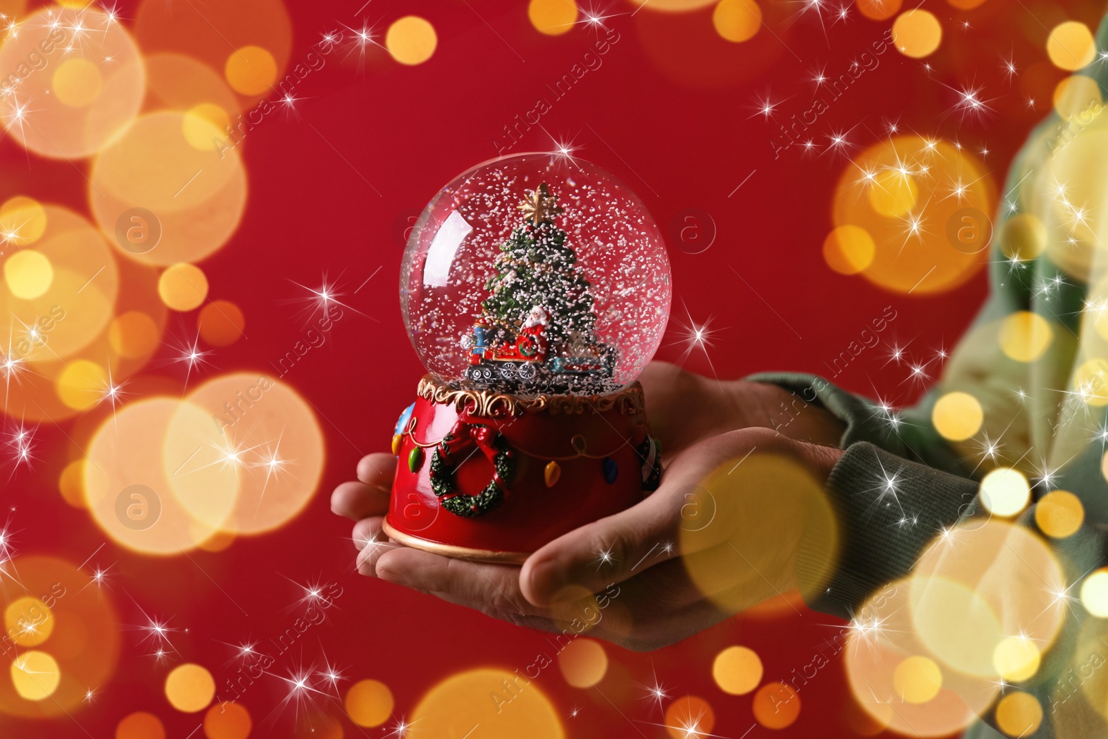 Image of Man holding snow globe on red background, closeup. Bokeh effect