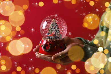 Man holding snow globe on red background, closeup. Bokeh effect