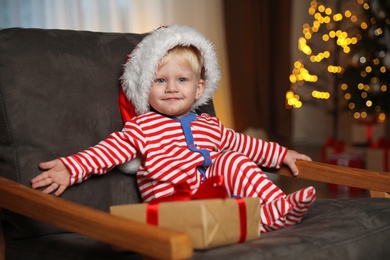 Baby in Christmas pajamas and Santa hat with gift box sitting in armchair at home