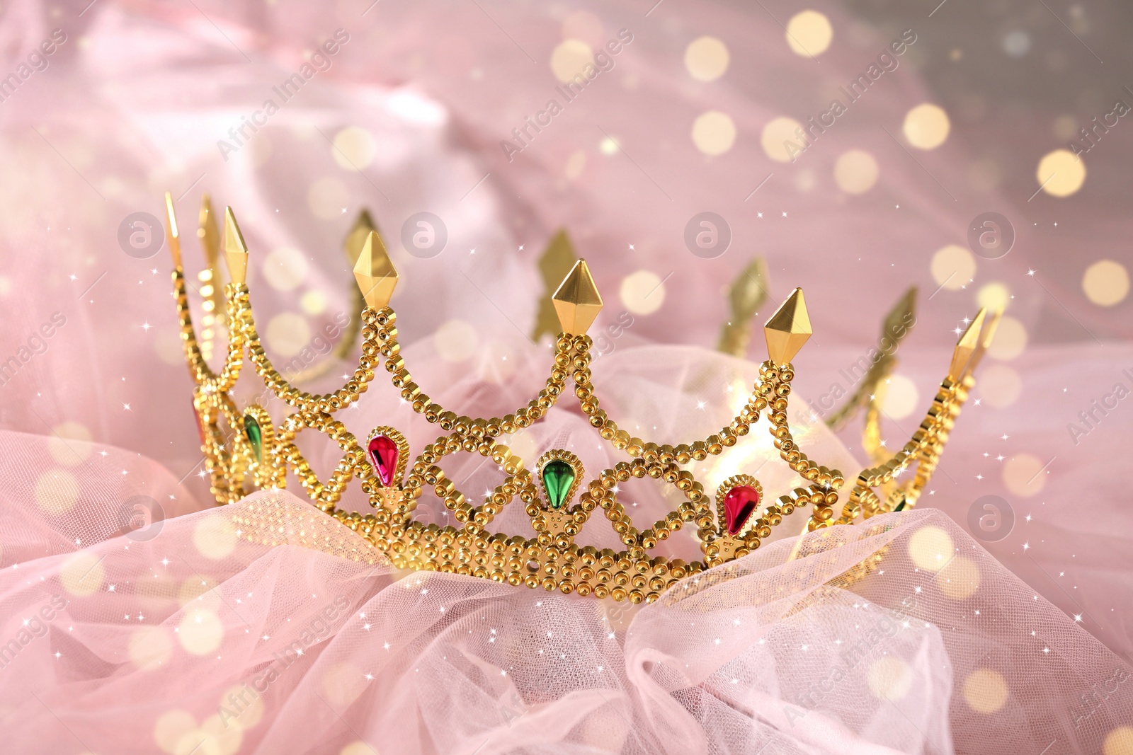 Image of Beautiful golden crown with gems on pink cloth, bokeh effect