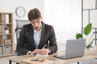 Man taking notes during webinar at wooden table indoors