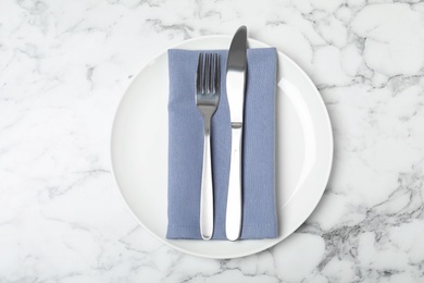 Photo of Plate with cutlery and napkin on marble background, top view