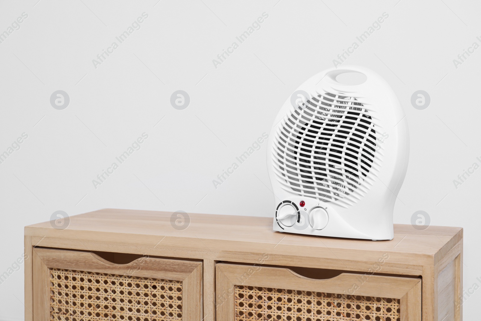 Photo of Electric fan heater on wooden cabinet indoors. Space for text