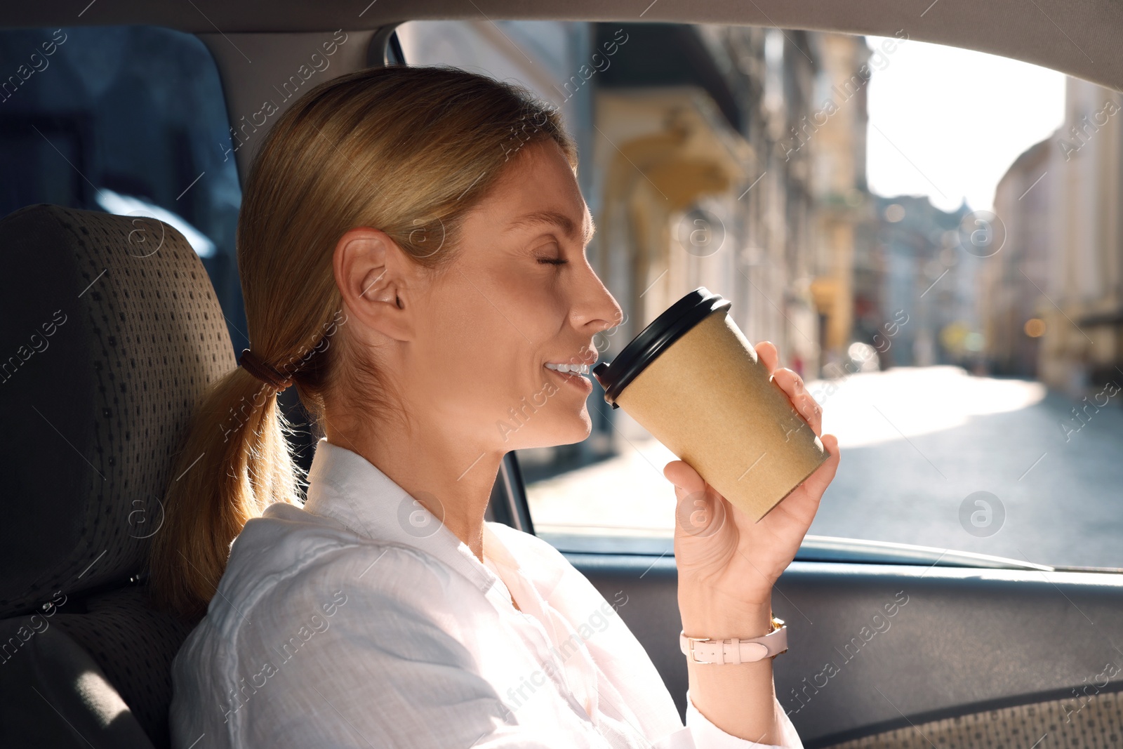 Photo of To-go drink. Happy woman drinking coffee in car