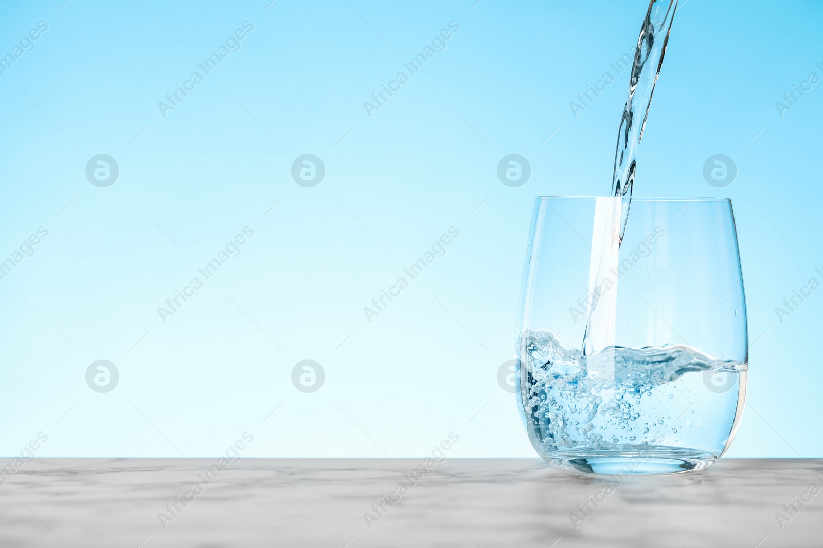 Photo of Pouring water into glass on blue background, space for text. Refreshing drink