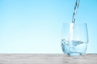 Pouring water into glass on blue background, space for text. Refreshing drink