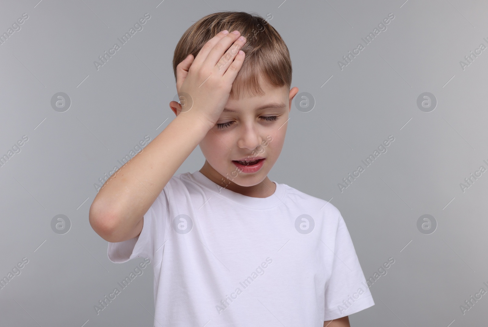 Photo of Little boy suffering from headache on grey background