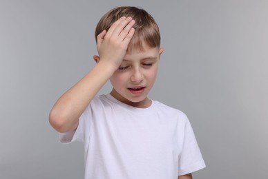 Little boy suffering from headache on grey background