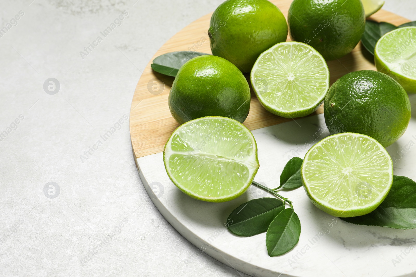 Photo of Fresh ripe limes and leaves on light table, closeup. Space for text