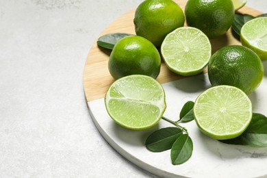 Fresh ripe limes and leaves on light table, closeup. Space for text