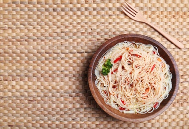 Photo of Bowl of delicious noodles with broth and vegetables on wicker background, top view. Space for text