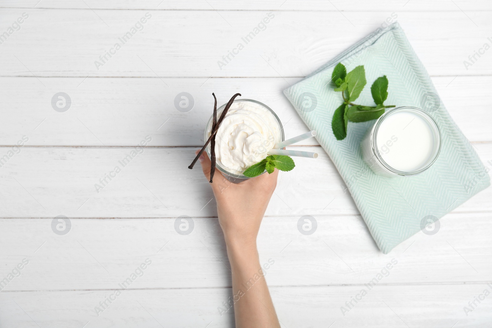 Photo of Woman holding glass of delicious milk shake with whipped cream at table, top view