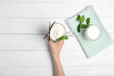 Woman holding glass of delicious milk shake with whipped cream at table, top view